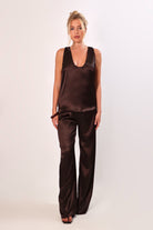 Model wearing a brown satin sleeveless top with a deep plunging neckline and matching satin pants for a sleek monochrome look.