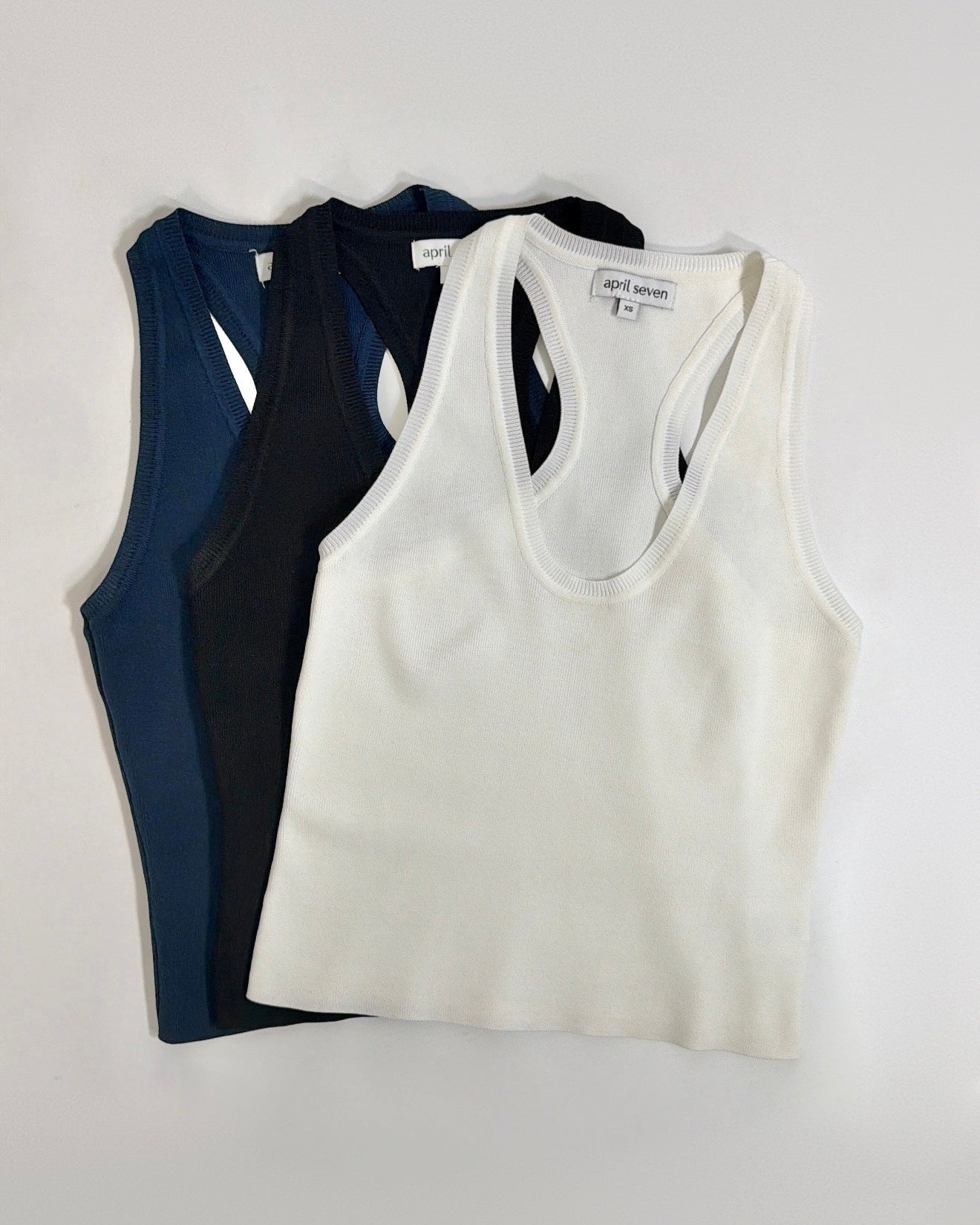 three tank tops, one navy, one black and one white, on a light gray background.