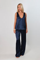 Model wearing a navy satin sleeveless top with a deep plunging neckline and relaxed fit, styled with matching satin pants against a neutral background.