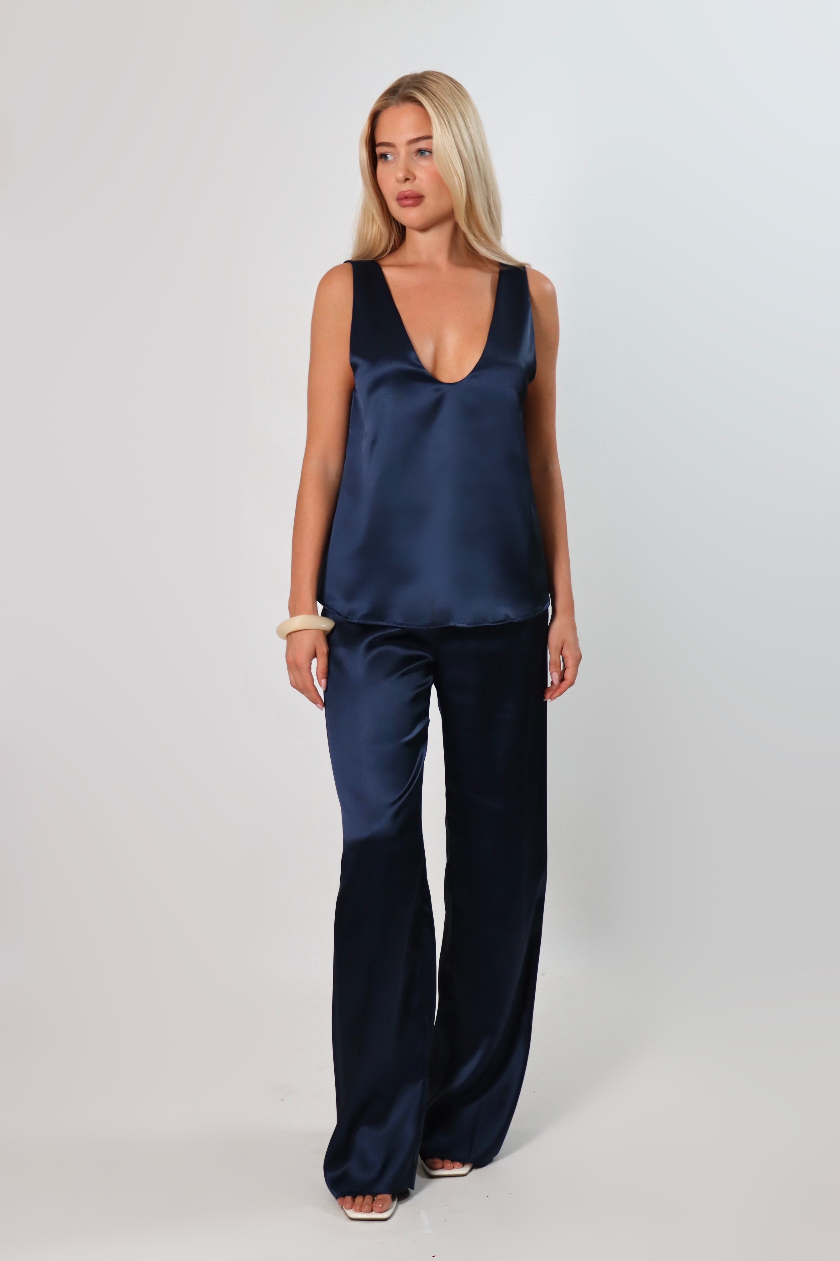 Model wearing a navy satin sleeveless top with a deep plunging neckline and relaxed fit, styled with matching satin pants against a neutral background.