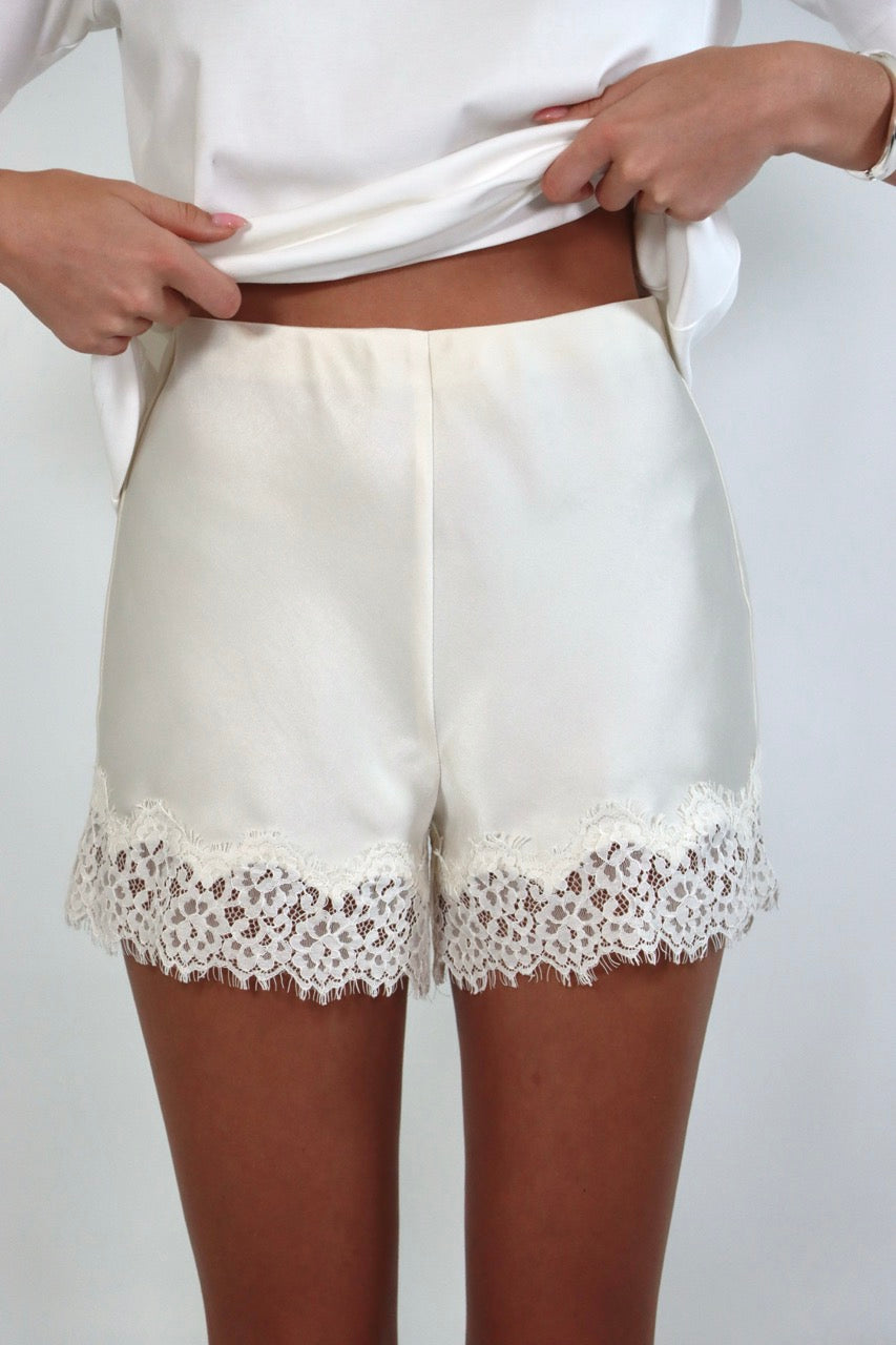 Woman wearing a relaxed white crewneck tee paired with ivory satin shorts featuring delicate lace trim.