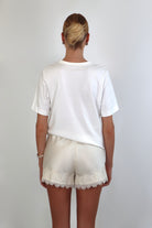 Woman wearing a relaxed white crewneck tee paired with ivory satin shorts featuring delicate lace trim.