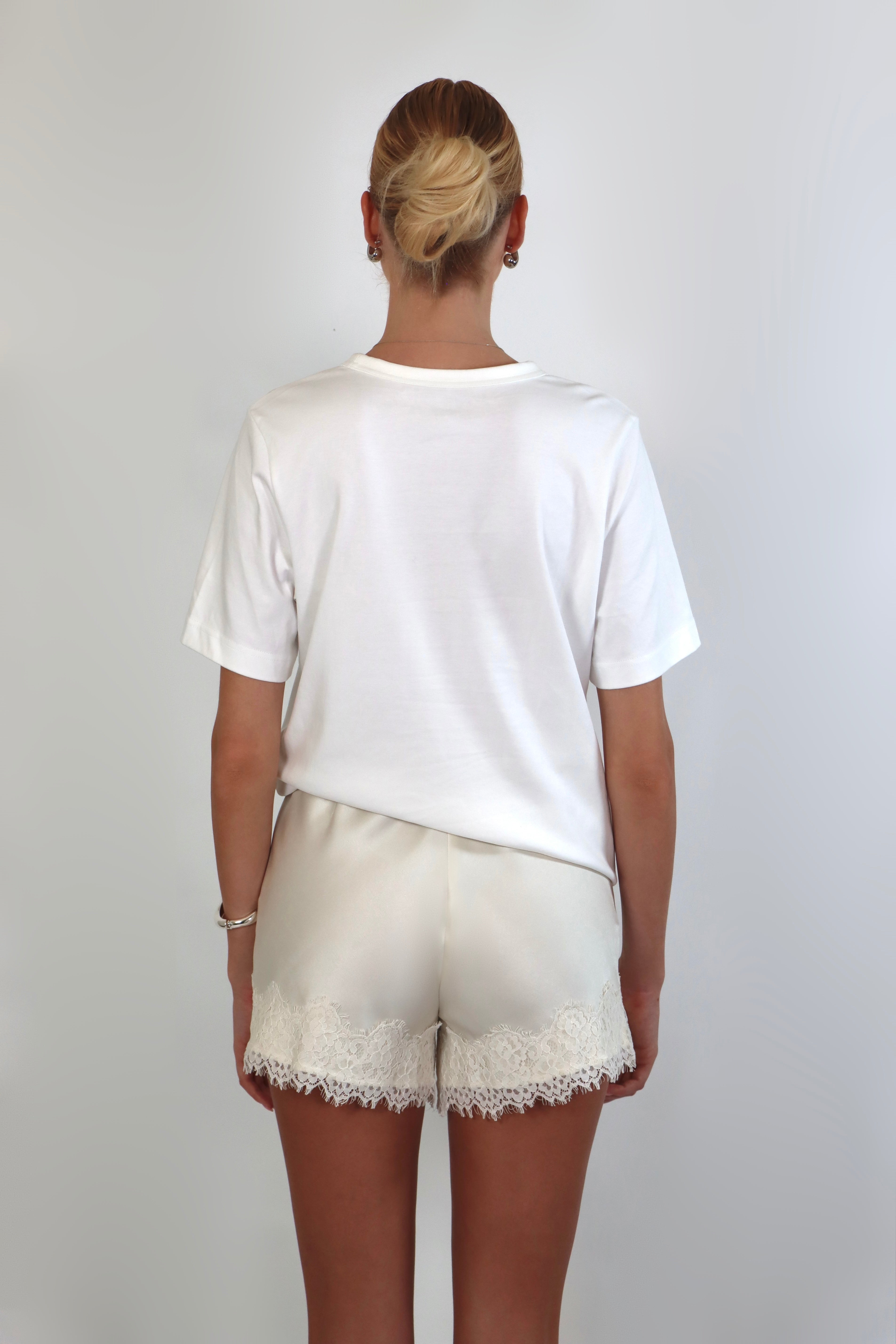 Woman wearing a relaxed white crewneck tee paired with ivory satin shorts featuring delicate lace trim.