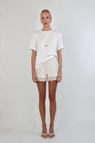 Woman wearing a relaxed white crewneck tee paired with ivory satin shorts featuring delicate lace trim.