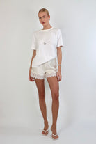 Woman wearing a relaxed white crewneck tee paired with ivory satin shorts featuring delicate lace trim.
