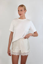Woman wearing a relaxed white crewneck tee paired with ivory satin shorts featuring delicate lace trim.