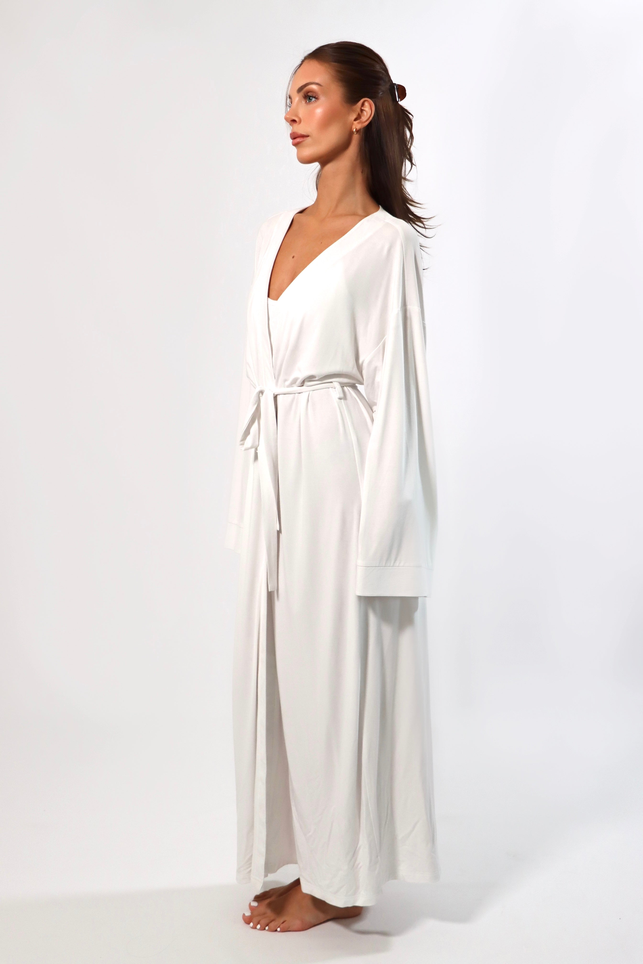 Woman in a white maxi robe with bell sleeves and tie waist. Side view.
