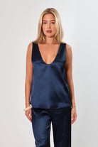 Model wearing a navy satin sleeveless top with a deep plunging neckline and relaxed fit, styled with matching satin pants against a neutral background.