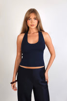 A woman wearing the Freya Tank, featuring a deep scoop neckline and a fitted racerback silhouette. The image highlights the fine rib fabrication and the body-skimming fit of the top in a neutral setting.