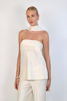 A model wearing a cream-colored, strapless satin top with a matching scarf wrapped elegantly around her neck. The top has a clean, structured bodice and is paired with matching April Satin Pants for a monochromatic, sophisticated look against a plain white background.