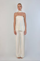 A model wearing a cream-colored, strapless satin top with a matching scarf wrapped elegantly around her neck. The top has a clean, structured bodice and is paired with matching April Satin Pants for a monochromatic, sophisticated look against a plain white background.