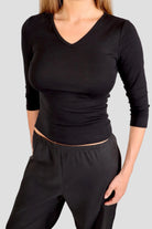 Woman wearing a black 3/4-sleeve top with V neckline and black pants against a plain background