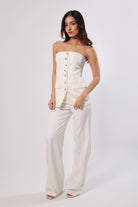 Woman in white strapless button-front vest top and wide-leg trousers.