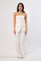 Woman in a white strapless button-front top and wide-leg pants.