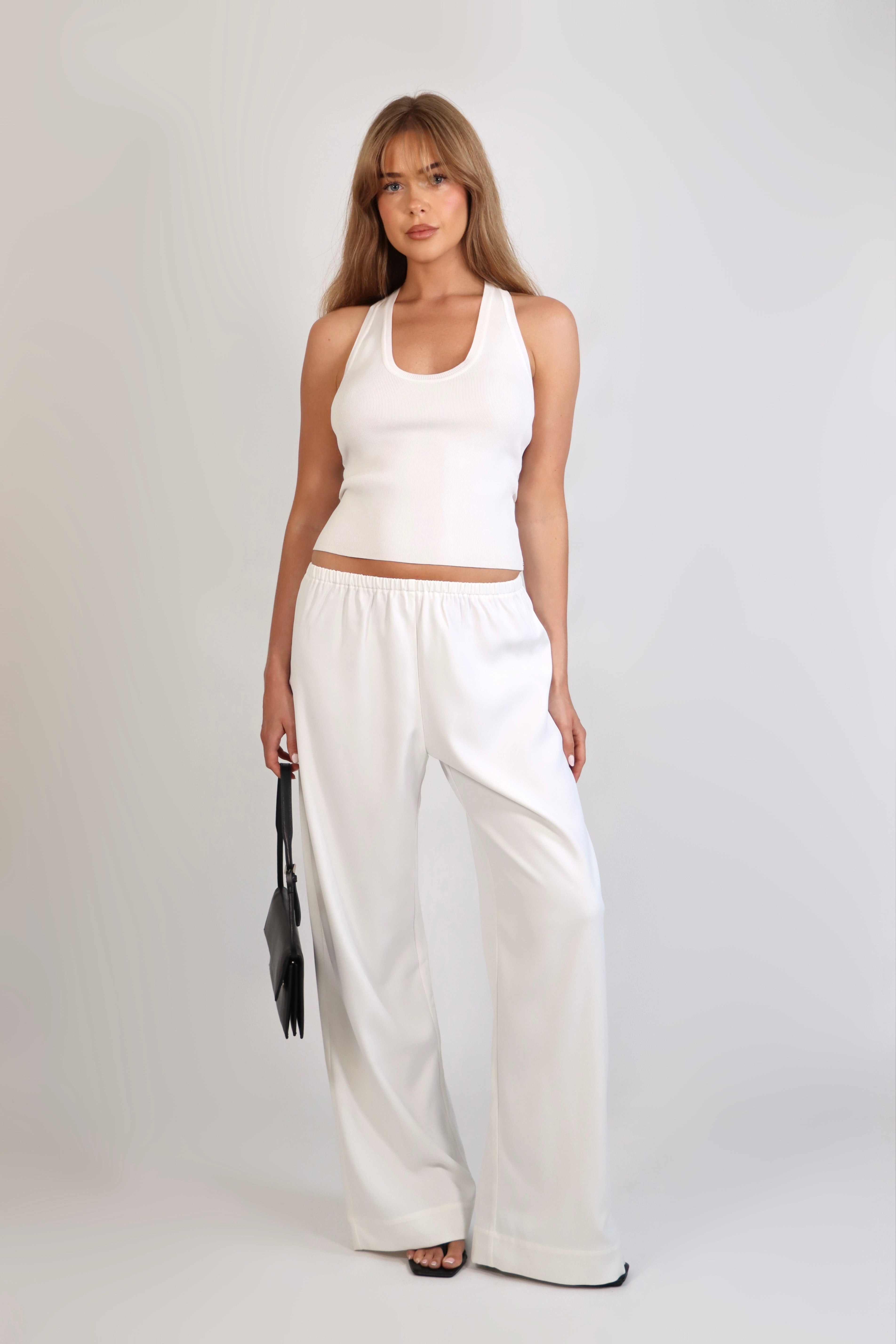 A woman wearing the Freya Tank, featuring a deep scoop neckline and a fitted racerback silhouette. The image highlights the fine rib fabrication and the body-skimming fit of the top in a neutral setting.