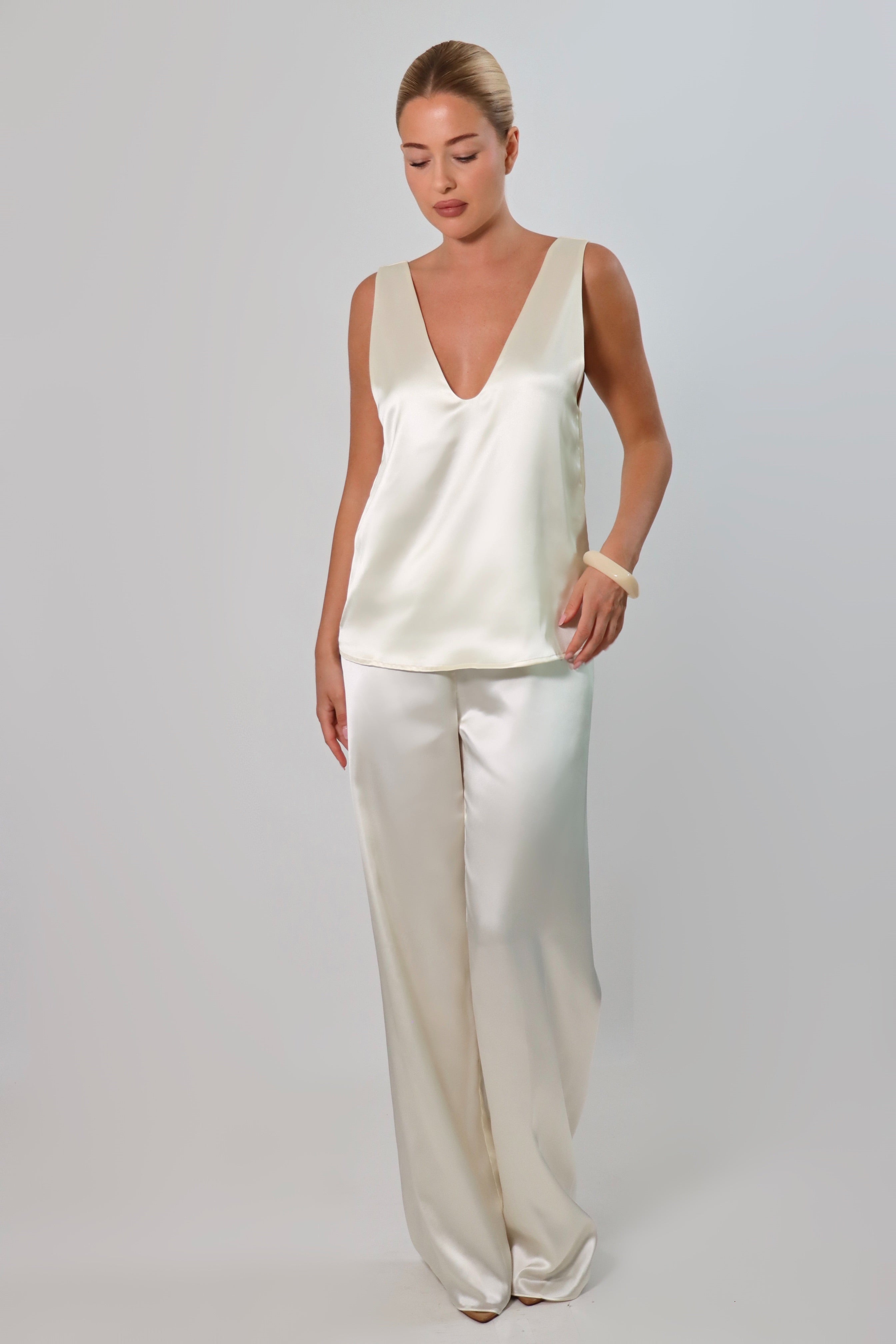 Ivory: Model wearing an ivory satin sleeveless top with a deep plunging neckline and matching satin pants against a neutral background.