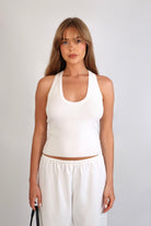 A woman wearing the Freya Tank, featuring a deep scoop neckline and a fitted racerback silhouette. The image highlights the fine rib fabrication and the body-skimming fit of the top in a neutral setting.